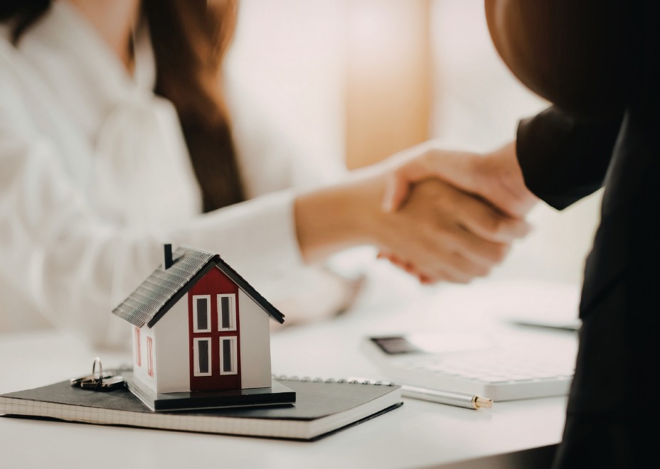 A real estate consultation handshake with a house model on the table